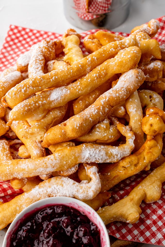 powdered sugar sprinkled funnel cake fries in a tissue paper lined basket