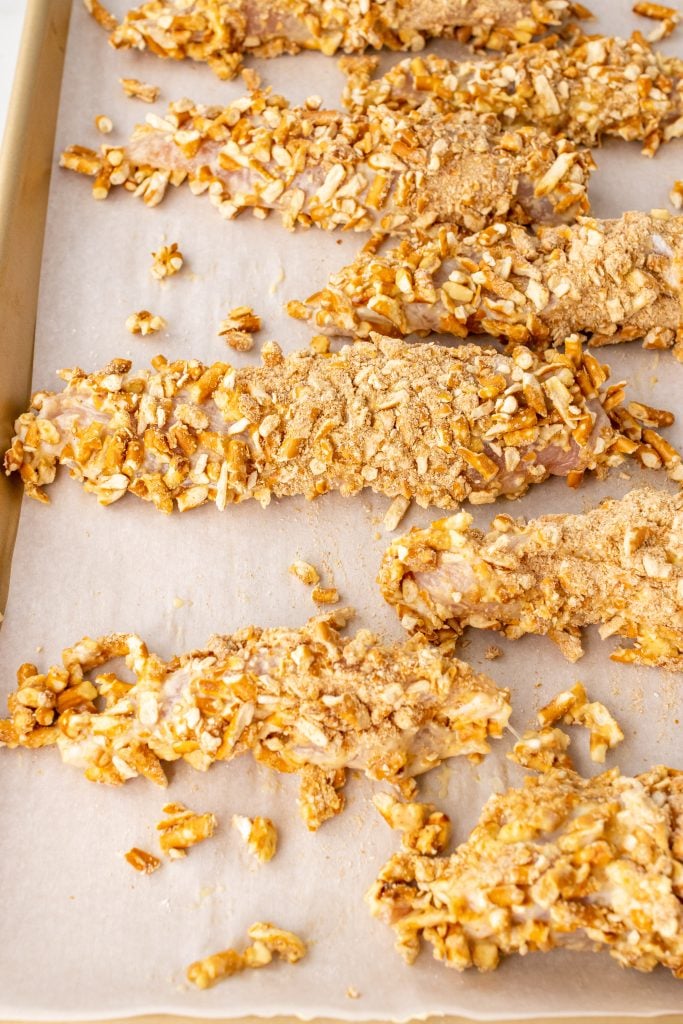 unbaked pretzel chicken tenders laid out on a parchment paper lined baking sheet
