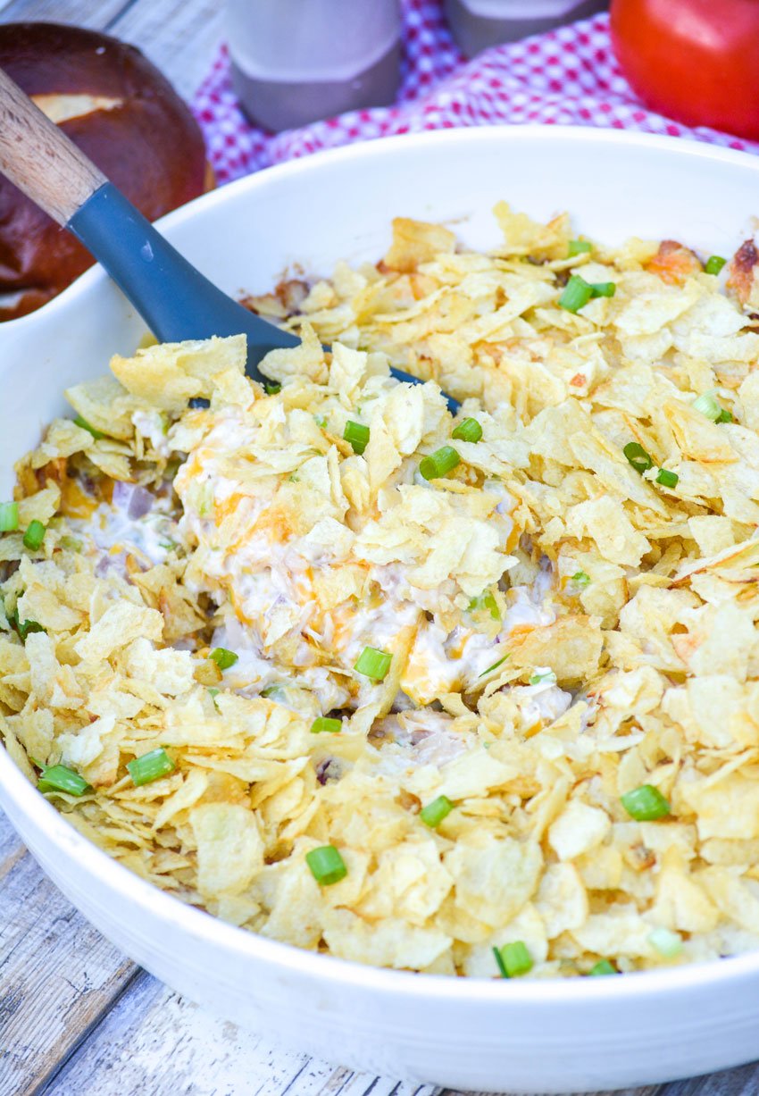 a serving spoon digging into a bowl of hot potato chip chicken salad casserole