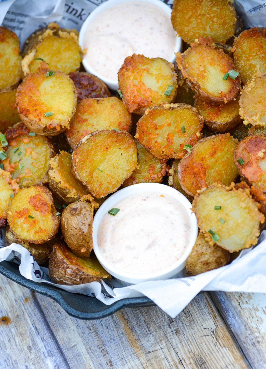 crispy parmesan crusted potatoes in a cast iron skillet with small white bowls of dip