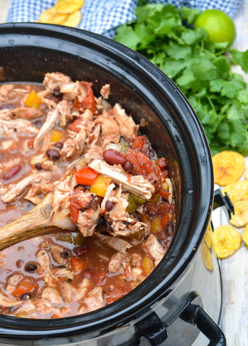 a wooden spoon holding up a spoonful of jerk chicken chili in a crockpot