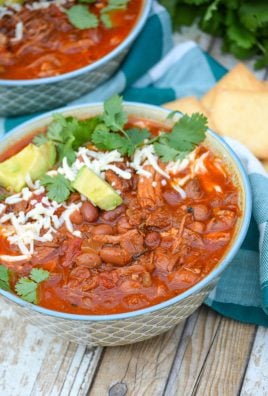 Slow cooker pulled pork chili in a blue bowl topped with cheese, cilantro leaves, and chunks of avocado