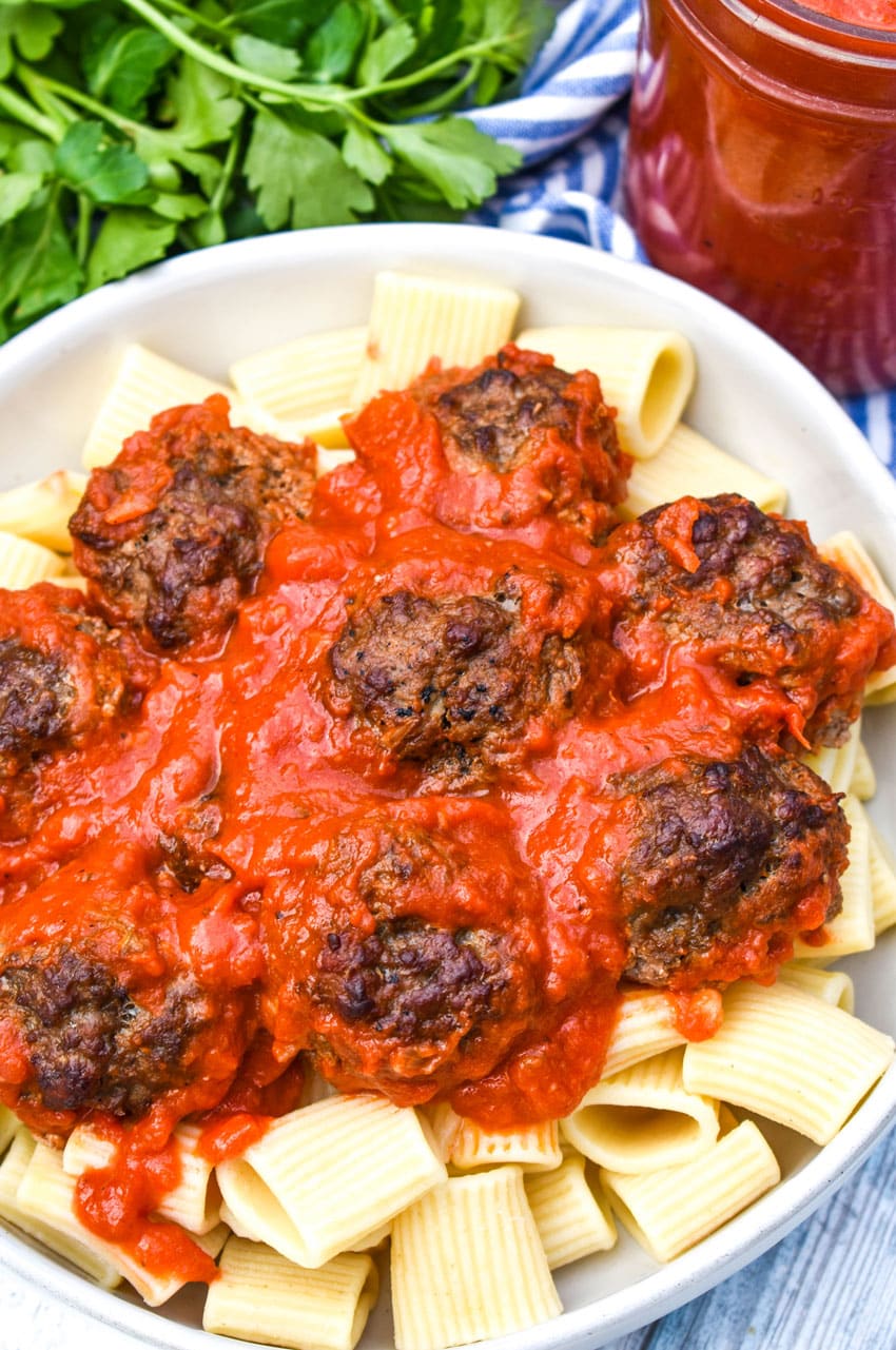 smoked meatballs in red sauce over cooked pasta in a white bowl