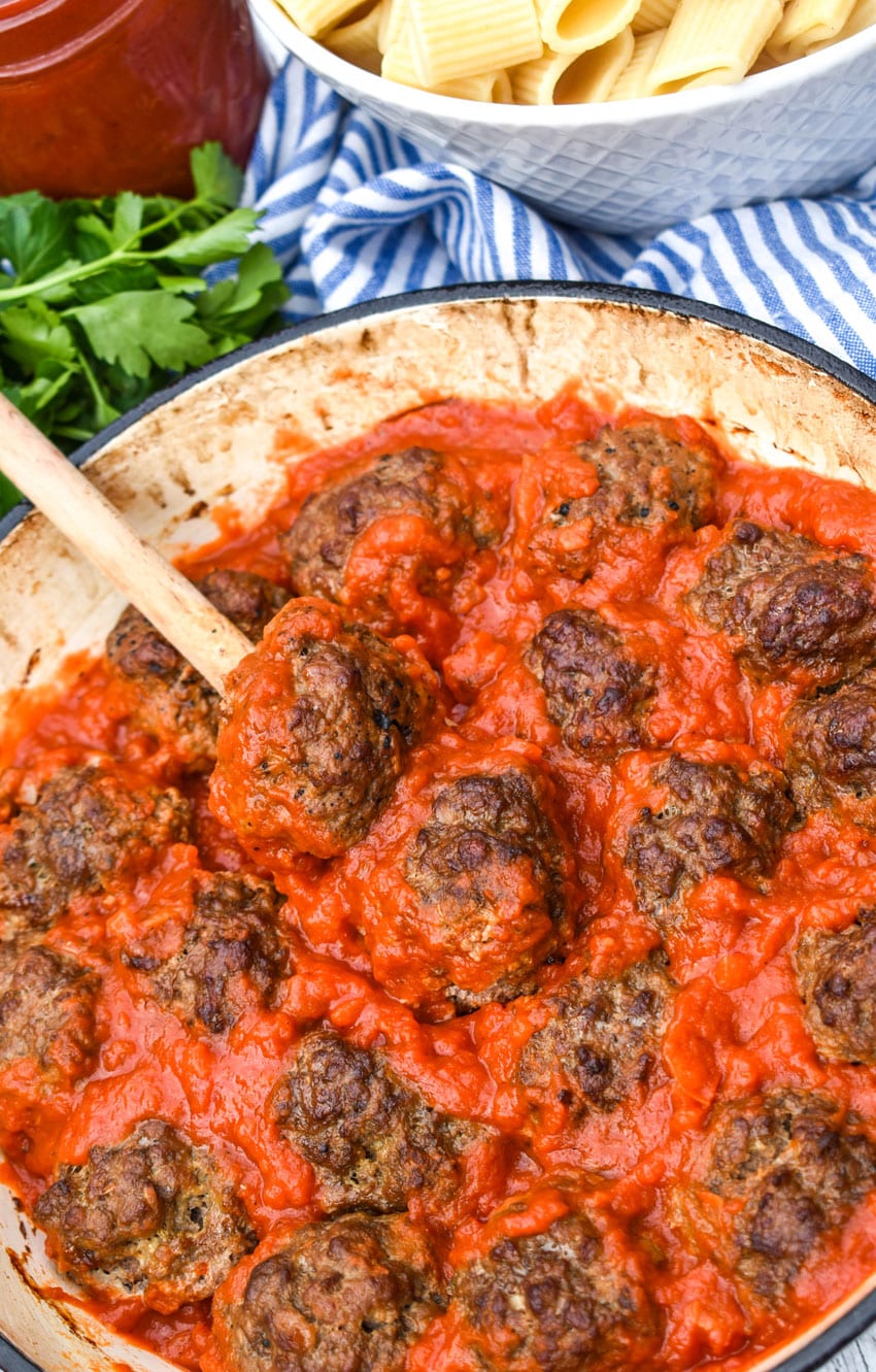 a wooden spoon scooping smoked meatballs in pasta sauce out of a cast iron skillet