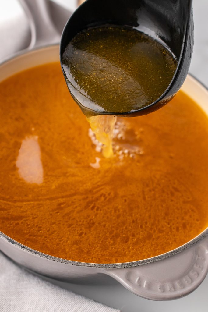 a black ladle pouring slow cooker chicken broth into a sauce pan