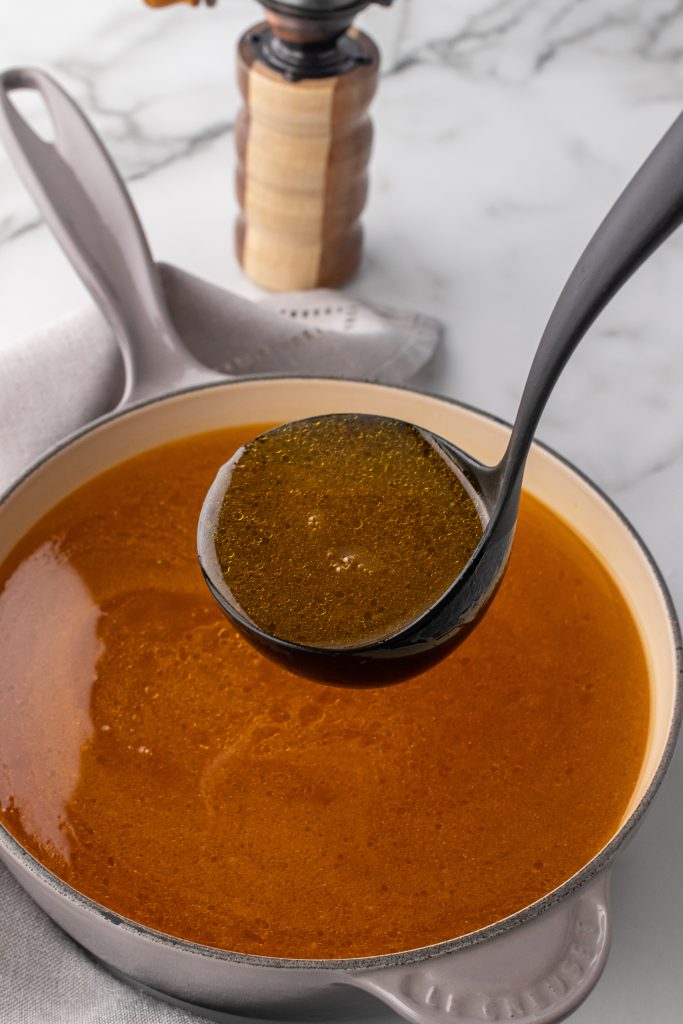 homemade bone broth in a black soup ladle held above a sauce pan
