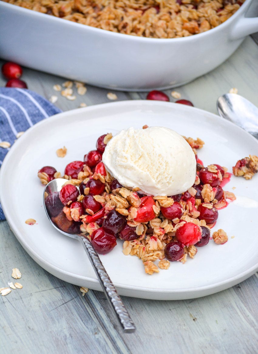cranberry crisp with oatmeal crumble topping on a white plate topped with a scoop of vanilla ice cream