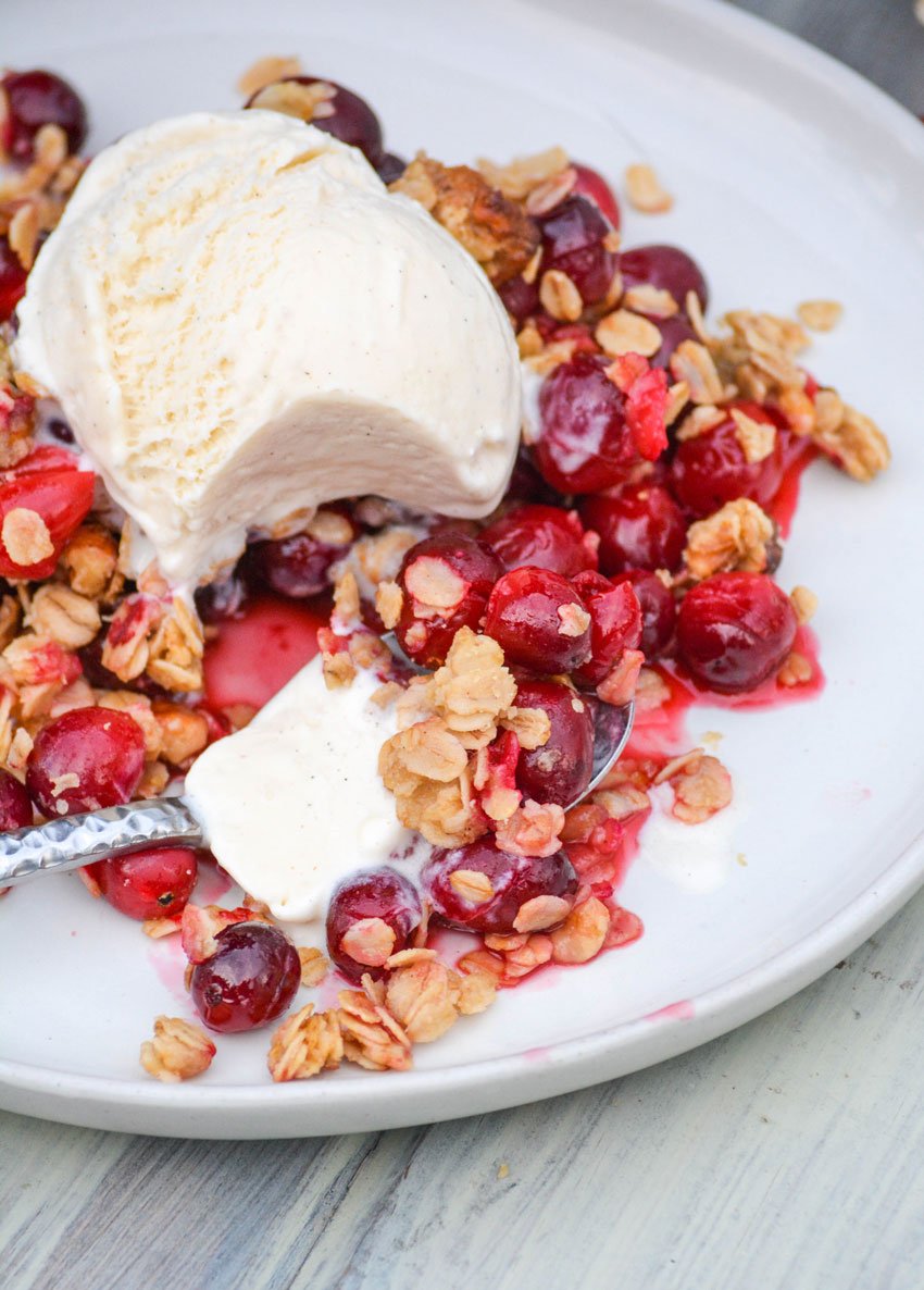 cranberry crisp with oatmeal crumble topping on a white plate topped with a scoop of vanilla ice cream