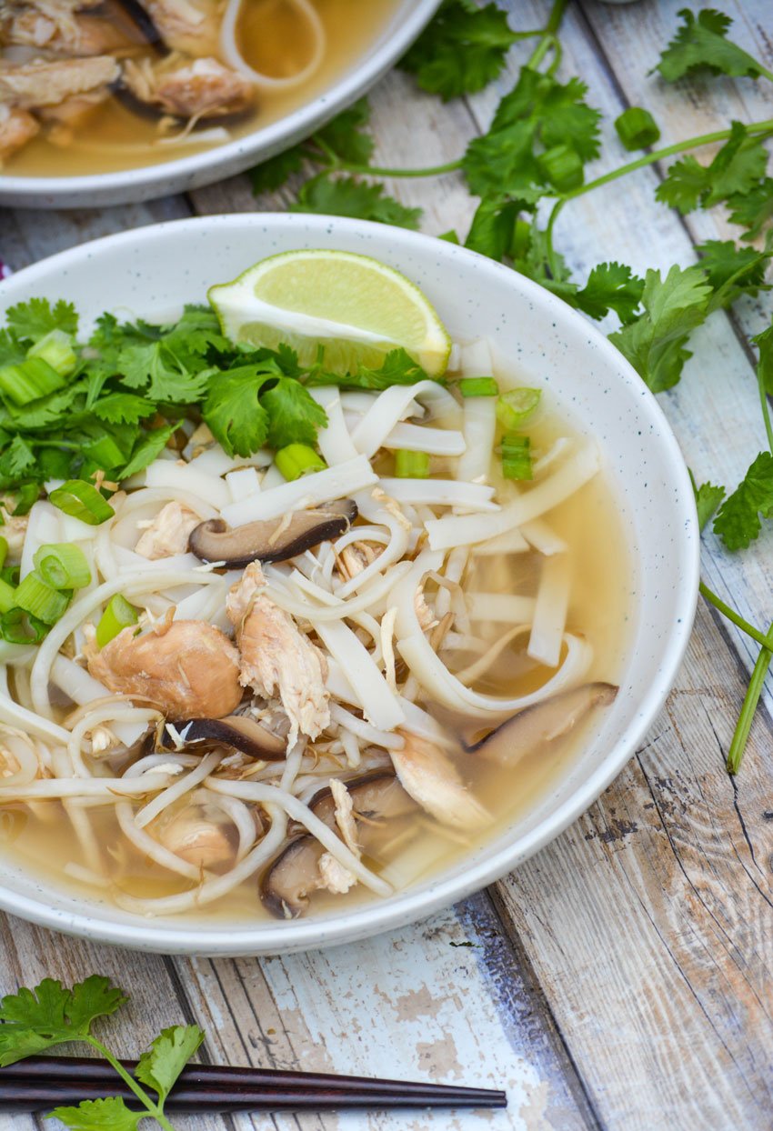 a white bowl filled with easy chicken pho topped with fresh cilantro leaves and a lime wedge