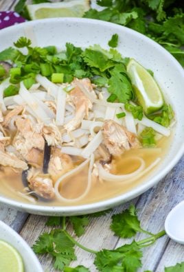 a white bowl filled with easy chicken pho topped with fresh cilantro leaves and a lime wedge