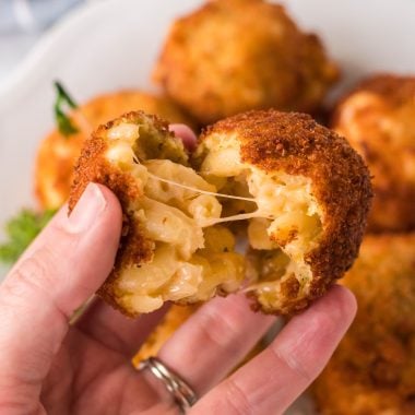 a hand holding up a split fried mac and cheese ball revealing the mac and cheese middle