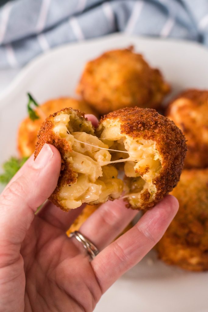 a hand holding up a split fried mac and cheese ball revealing the mac and cheese middle