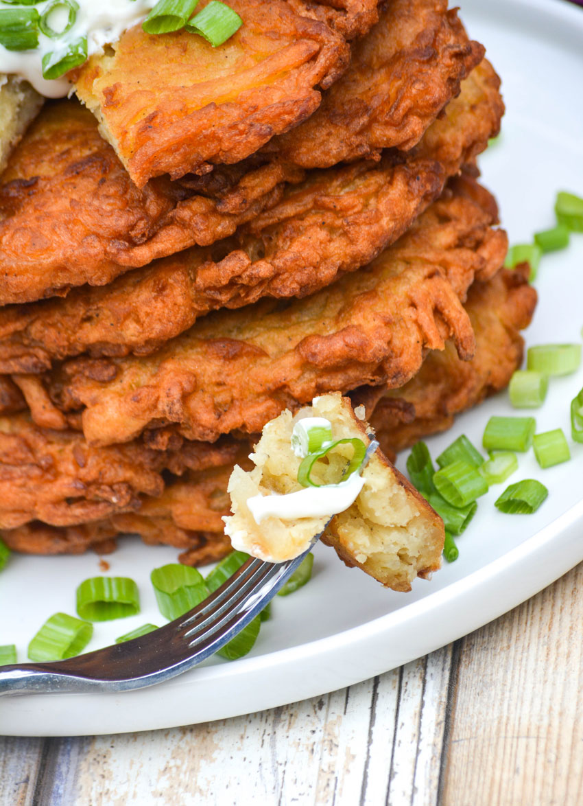 a silver fork resting on a white plate with a sour cream topped piece of potato latke pancake
