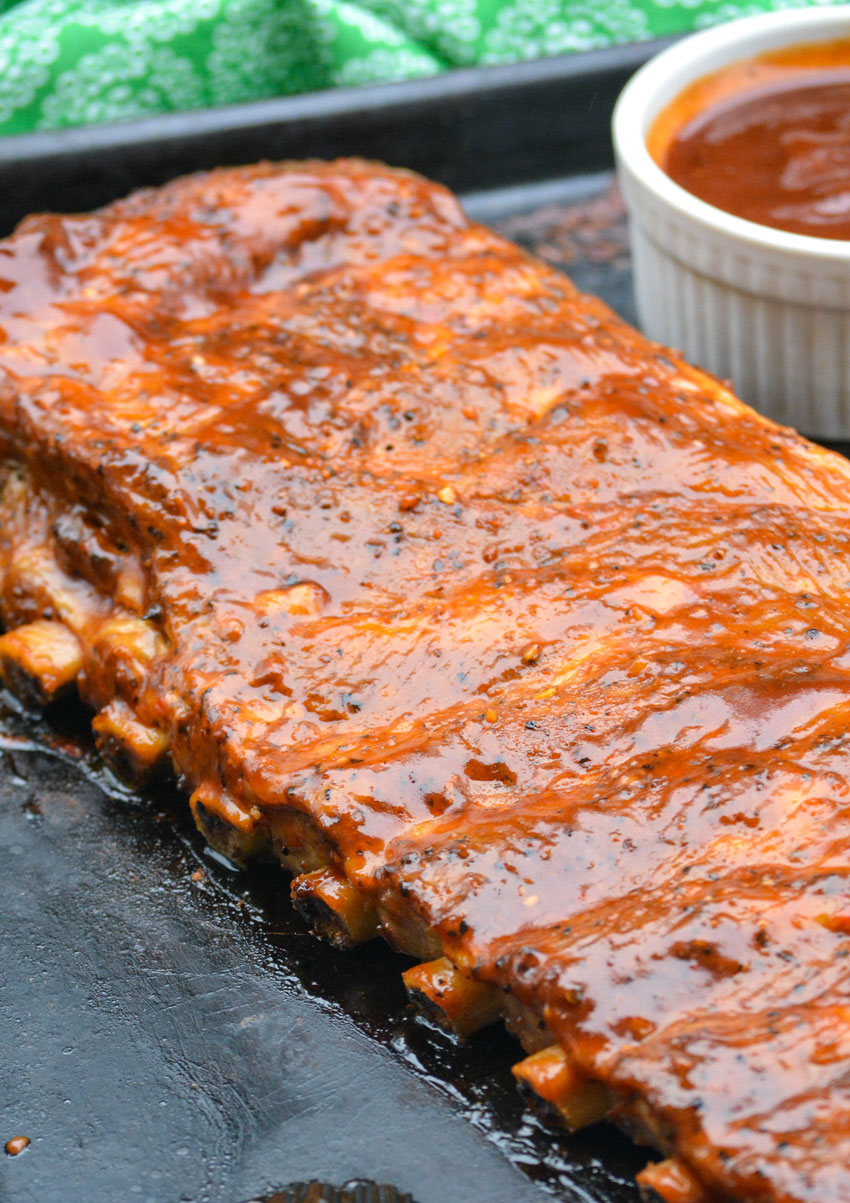a barbecue sauced cooked rack of ribs on a metal baking pan