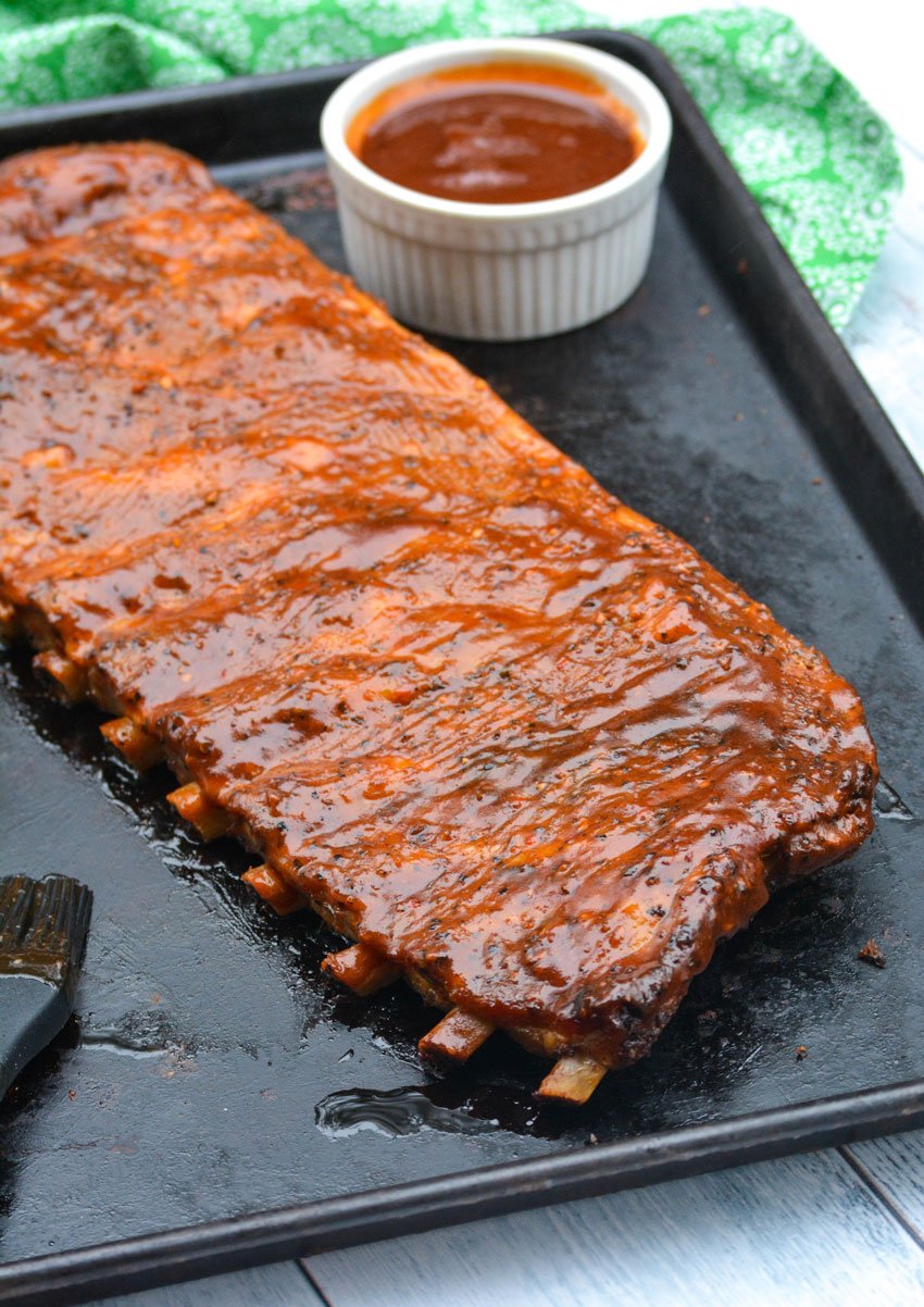 a barbecue sauced cooked rack of ribs on a metal baking pan