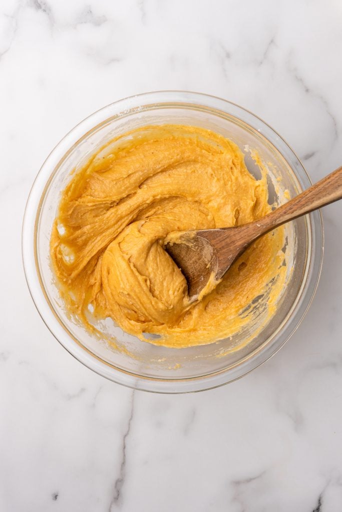 pumpkin cake batter in a glass mixing bowl with a wooden spoon