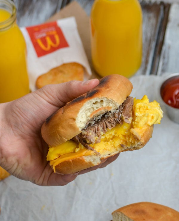 a hand holding up a copycat mcdonalds steak egg and cheese bagel with a bite taken out of it