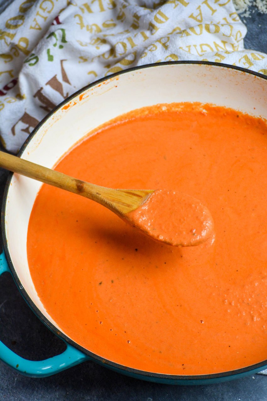 a wooden spoon lifting a scoop of easy homemade vodka sauce out of a shallow sauce pan