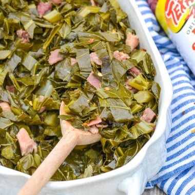 a wooden spoon in a white casserole dish filled with slow cooker collard greens with ham