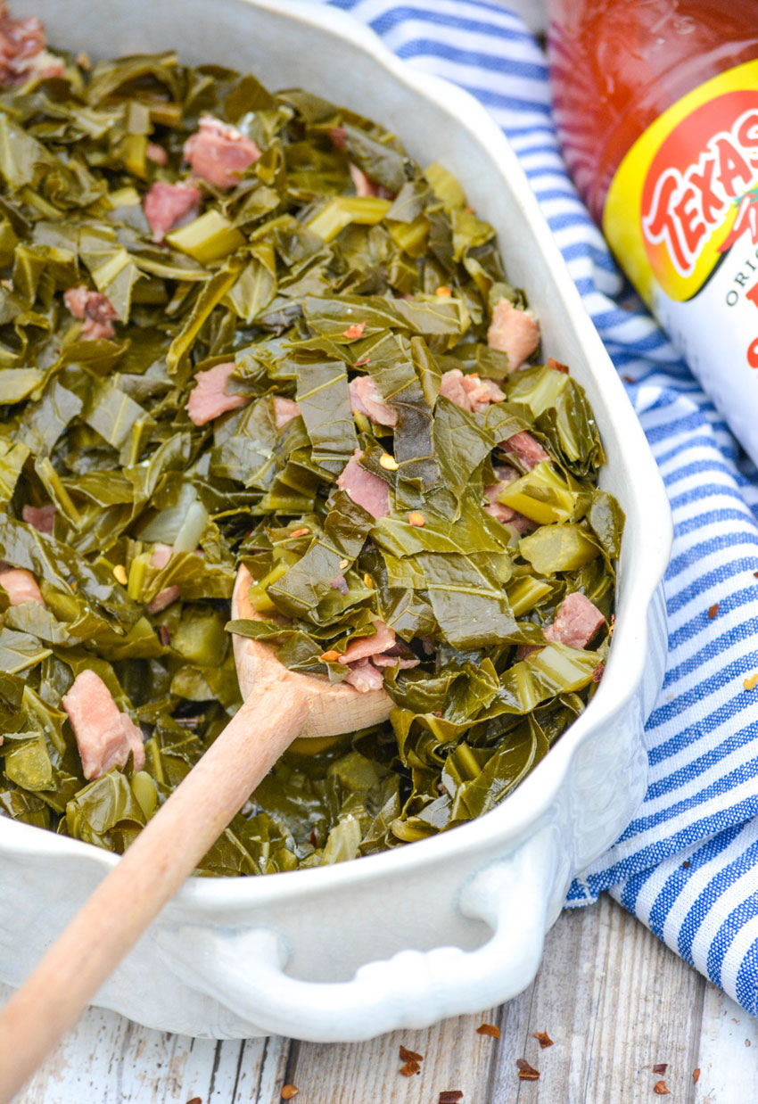 a wooden spoon in a white casserole dish filled with slow cooker collard greens with ham