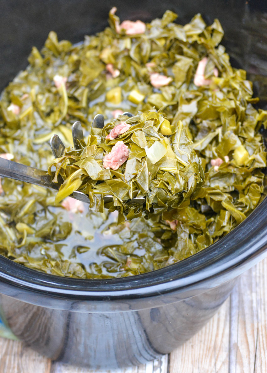 a silver spoon scooping crockpot collard greens out of the black bowl of a slow cooker