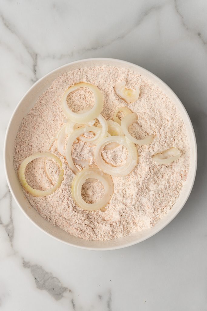 buttermilk dipped onions slices in a bowl of seasoned flour