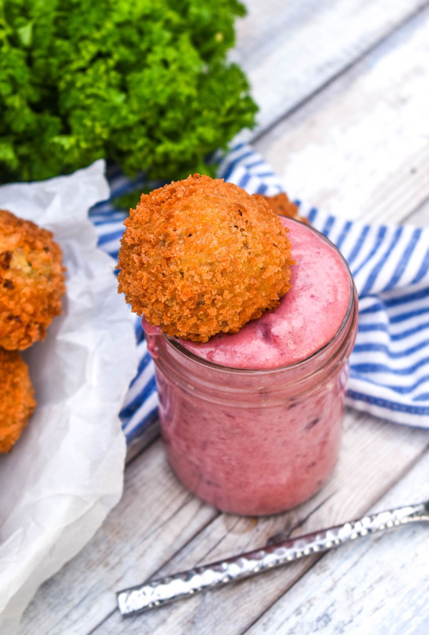 a deep fried cornbread stuffing ball in a glass of cranberry dipping sauce