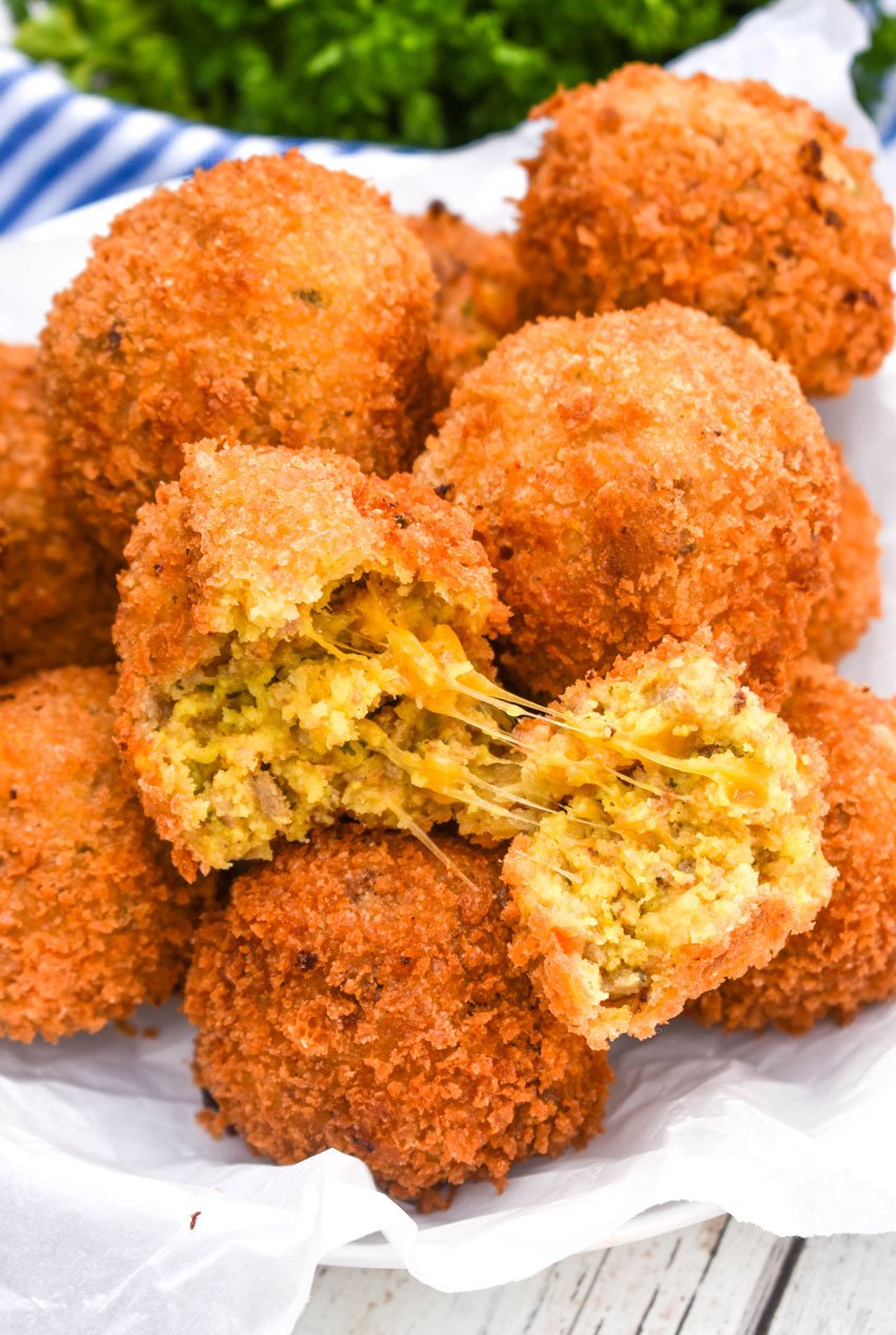a pile of deep fried cornbread stuffing balls with one torn open to reveal a cheesy center