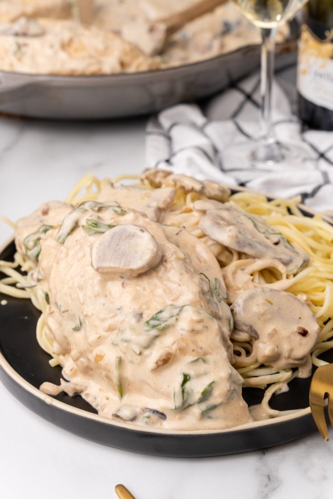 champagne chicken over cooked pasta on a black plate