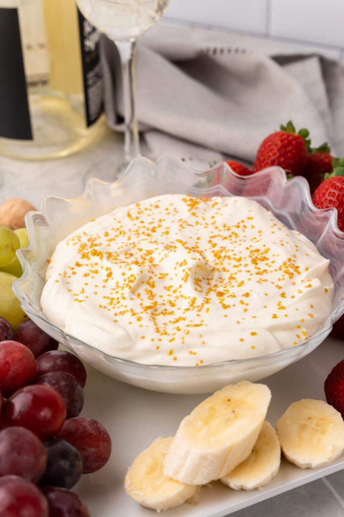 cheesecake fruit dip topped with golden sprinkles in a clear glass bowl