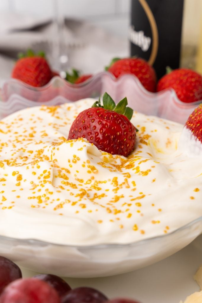 a strawberry in a golden sprinkle topped bowl of champagne cheesecake fruit dip
