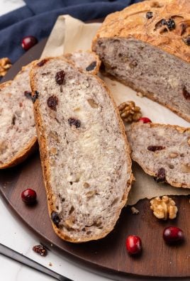 buttered slices of cranberry walnut dutch oven bread on a wooden cutting board