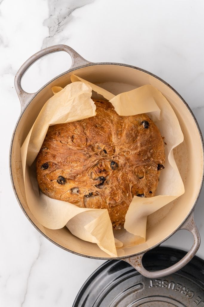 a loaf of baked cranberry walnut bread wrapped in parchment paper and sitting in a large dutch oven
