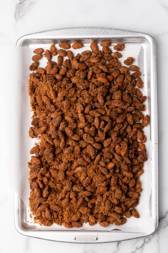 slow cooked cinnamon sugar almonds spread out on a parchment paper lined baking sheet