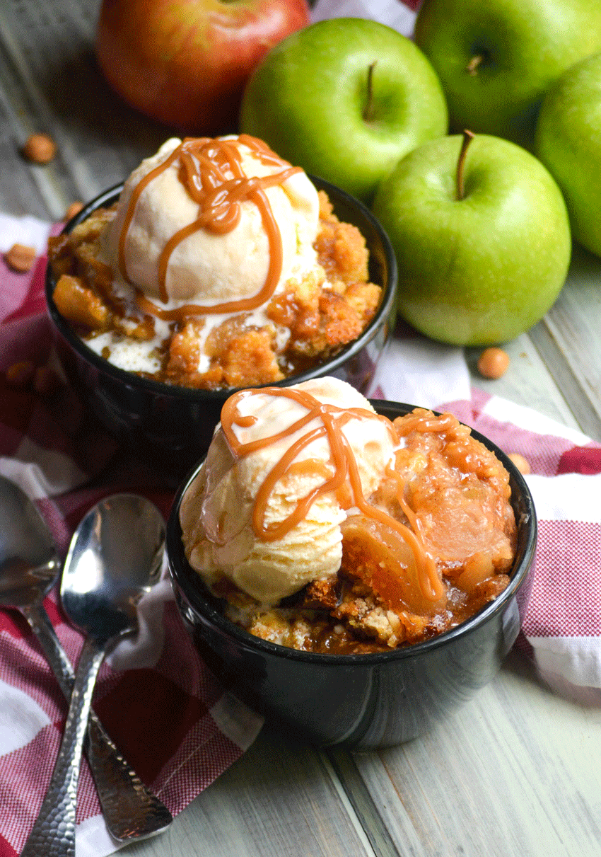 caramel apple dump cake in two black bowls topped with scoops of vanilla ice cream and caramel syrup