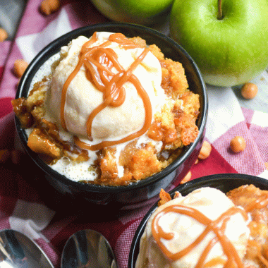 caramel apple dump cake in two black bowls topped with scoops of vanilla ice cream and caramel syrup