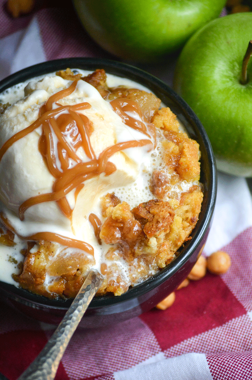 a silver spoon in a bowl of apple pie dump cake topped with melting vanilla ice cream and caramel syrup