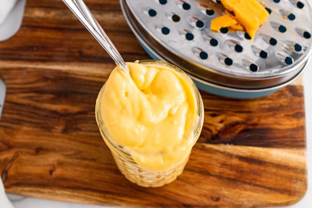 a spoon stuck in a glass jar filled with homemade cheese sauce
