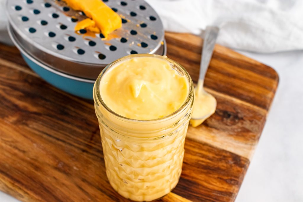 a glass jar filled with thick homemade cheese sauce sitting on a wooden cutting board