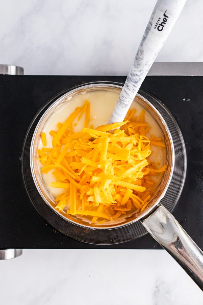 shredded cheese in a pot with white cream sauce and a spatula