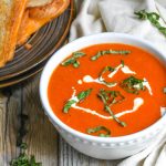 copycat panera tomato soup recipe in a white bowl topped with cream and fresh basil