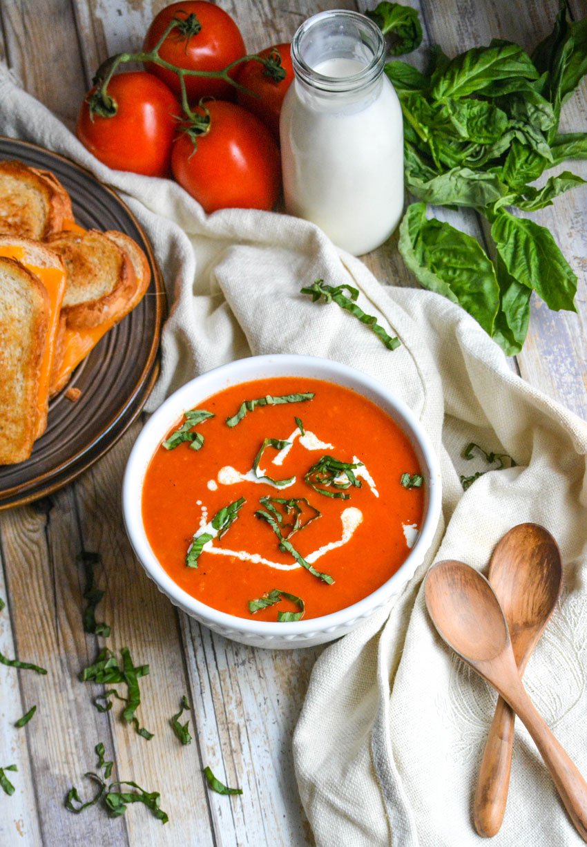 copycat panera tomato soup recipe in a white bowl topped with cream and fresh basil