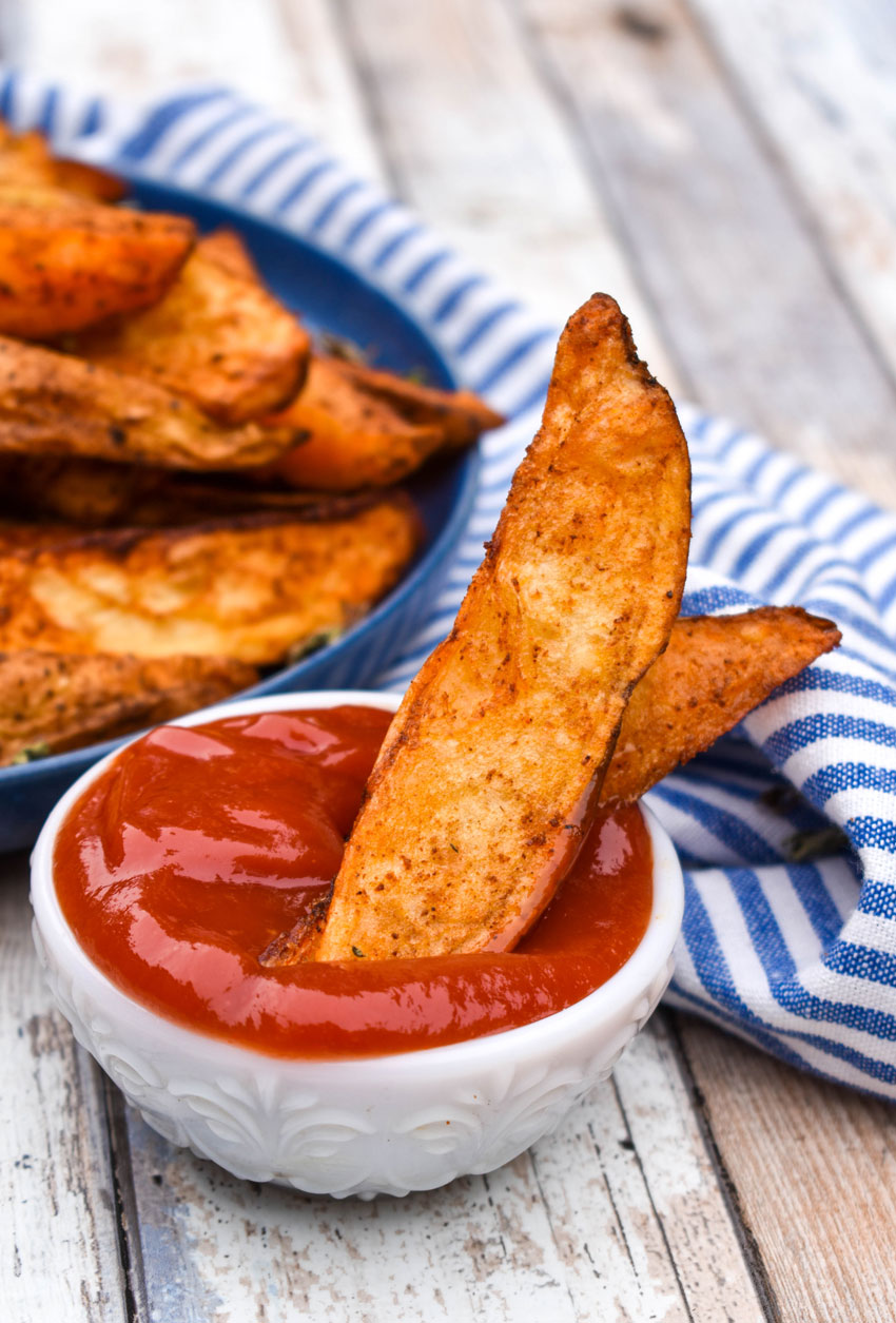 a crispy air fried potato wedge in a small white bowl filled with ketchup