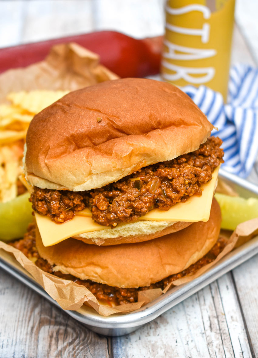 two sloppy joe cheeseburgers stacked on a metal tray lined with brown parchment paper