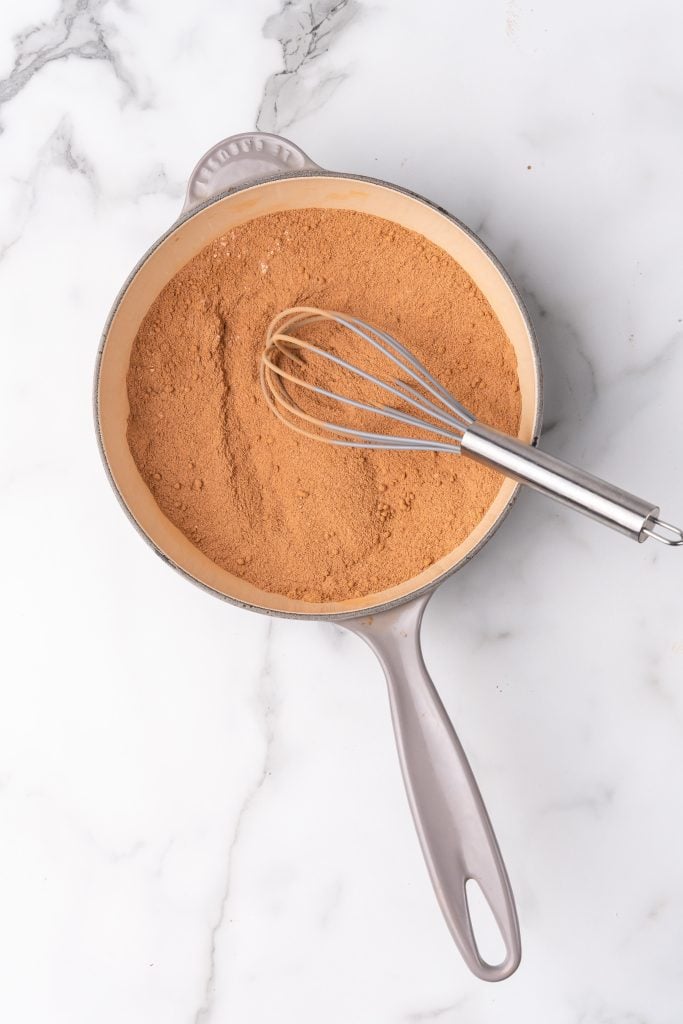 cocoa powder and a wire whisk in a gray sauce pan