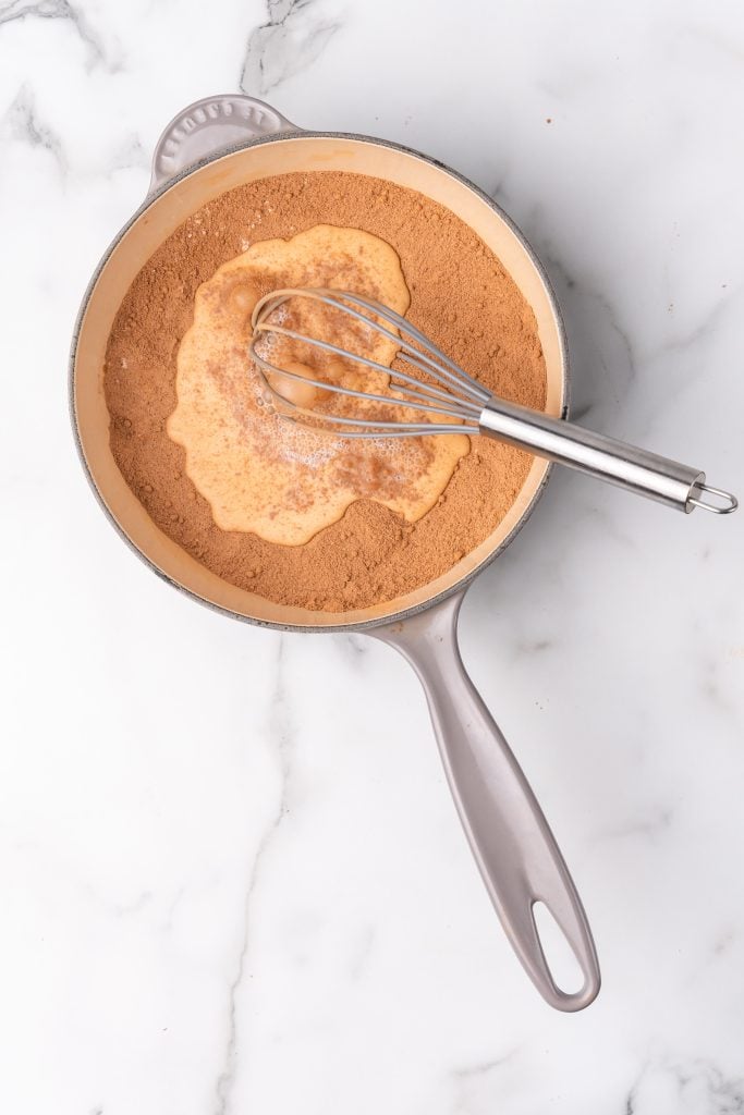 cocoa powder, milk, and a wire whisk in a gray sauce pan