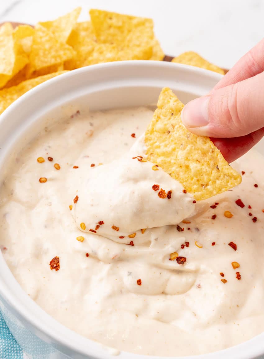 a hand dipping a tortilla chip in creamy mexican white ranch salsa