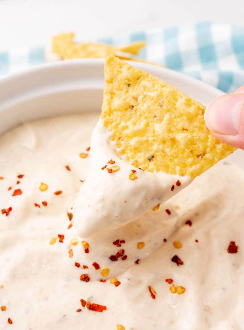 a hand dipping a tortilla chip in creamy mexican white ranch salsa