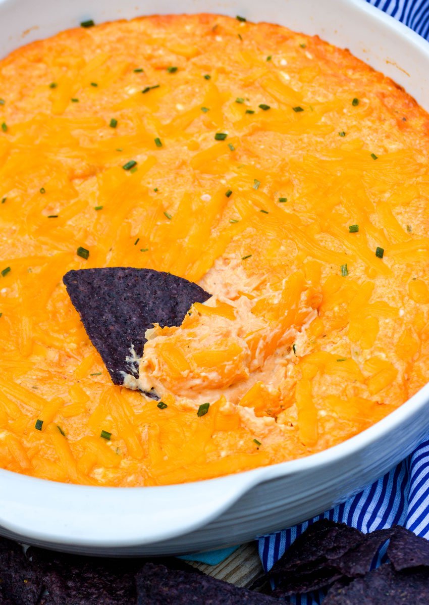 a blue corn tortilla chip dipped in the middle of a big bowl of creamy buffalo chicken dip