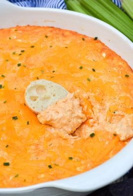 a baguette slice dipped in a white bowl of creamy buffalo chicken dip